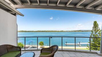 A balcony with a view of a lake, wicker furniture, and a clear sky.