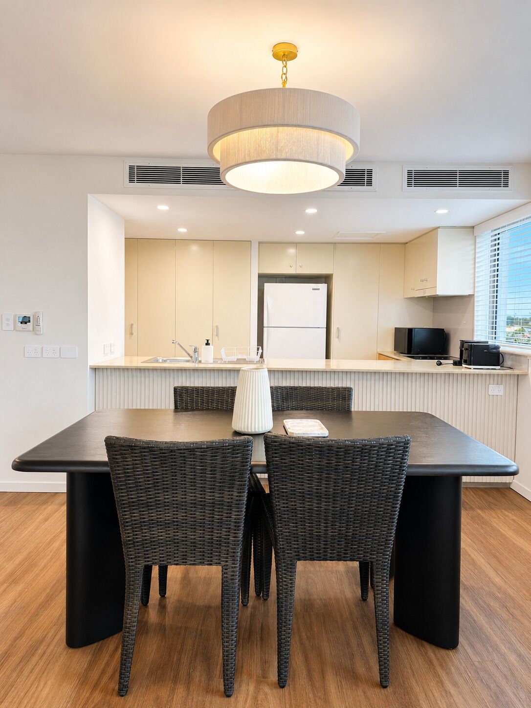 Une cuisine moderne avec un coin repas, comprenant une grande table, des chaises en osier et un luminaire central.