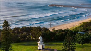 A lighthouse on a grassy hill overlooking a beach with waves crashing onto the shore. - Riverside Apartments & Hotel Ballina (Ballina)