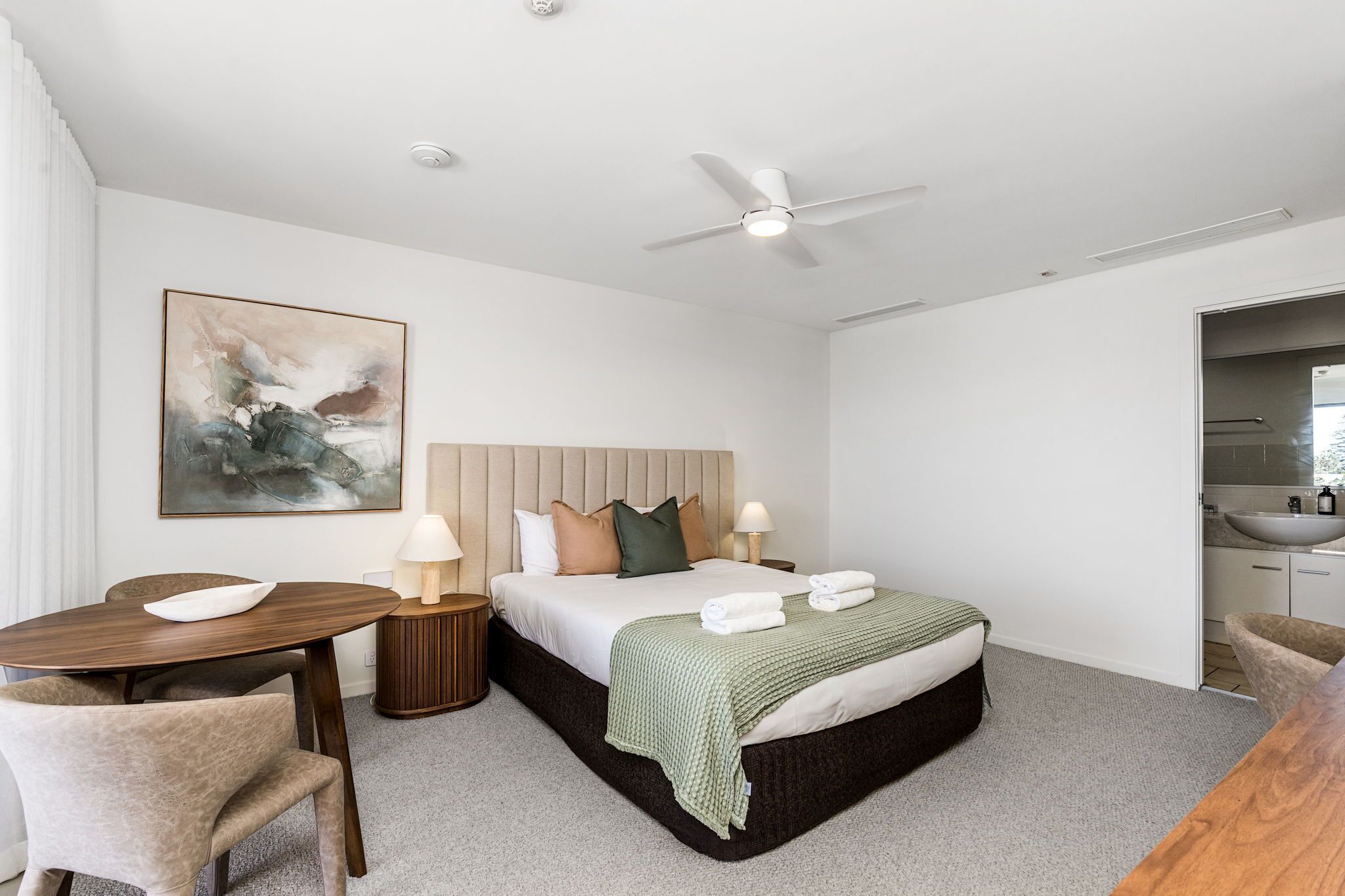 A hotel room with a bed, bedside table, lamp, and a painting on the wall.