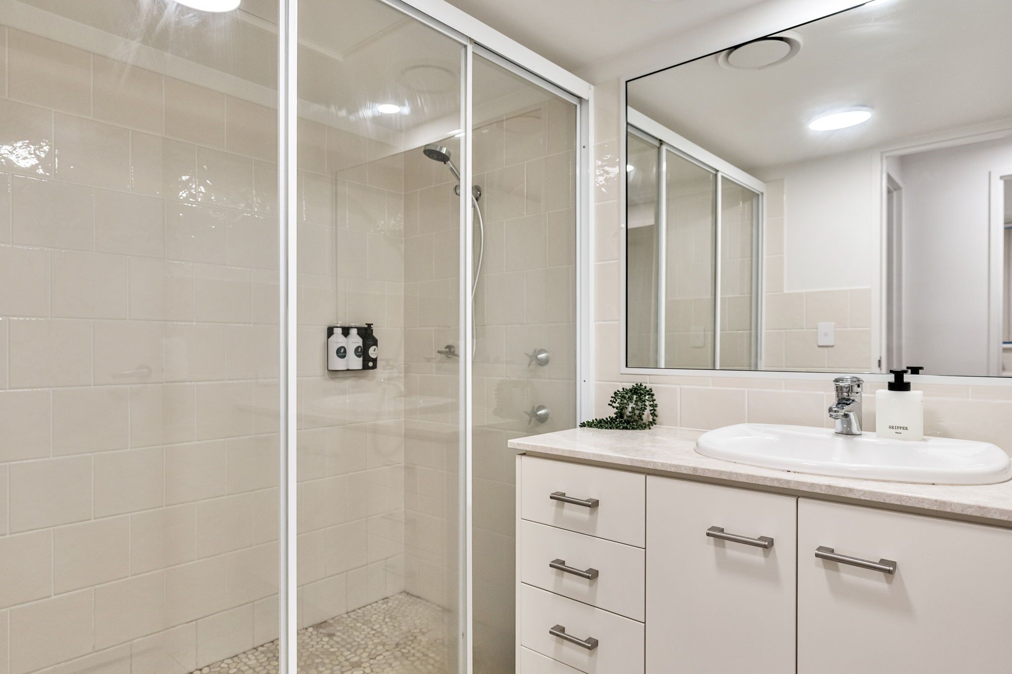 A modern bathroom with a glass shower enclosure, a white sink, and a large mirror.