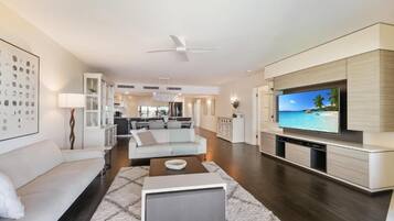 A modern living room with a flat-screen TV, a sofa, a coffee table, and a ceiling fan.