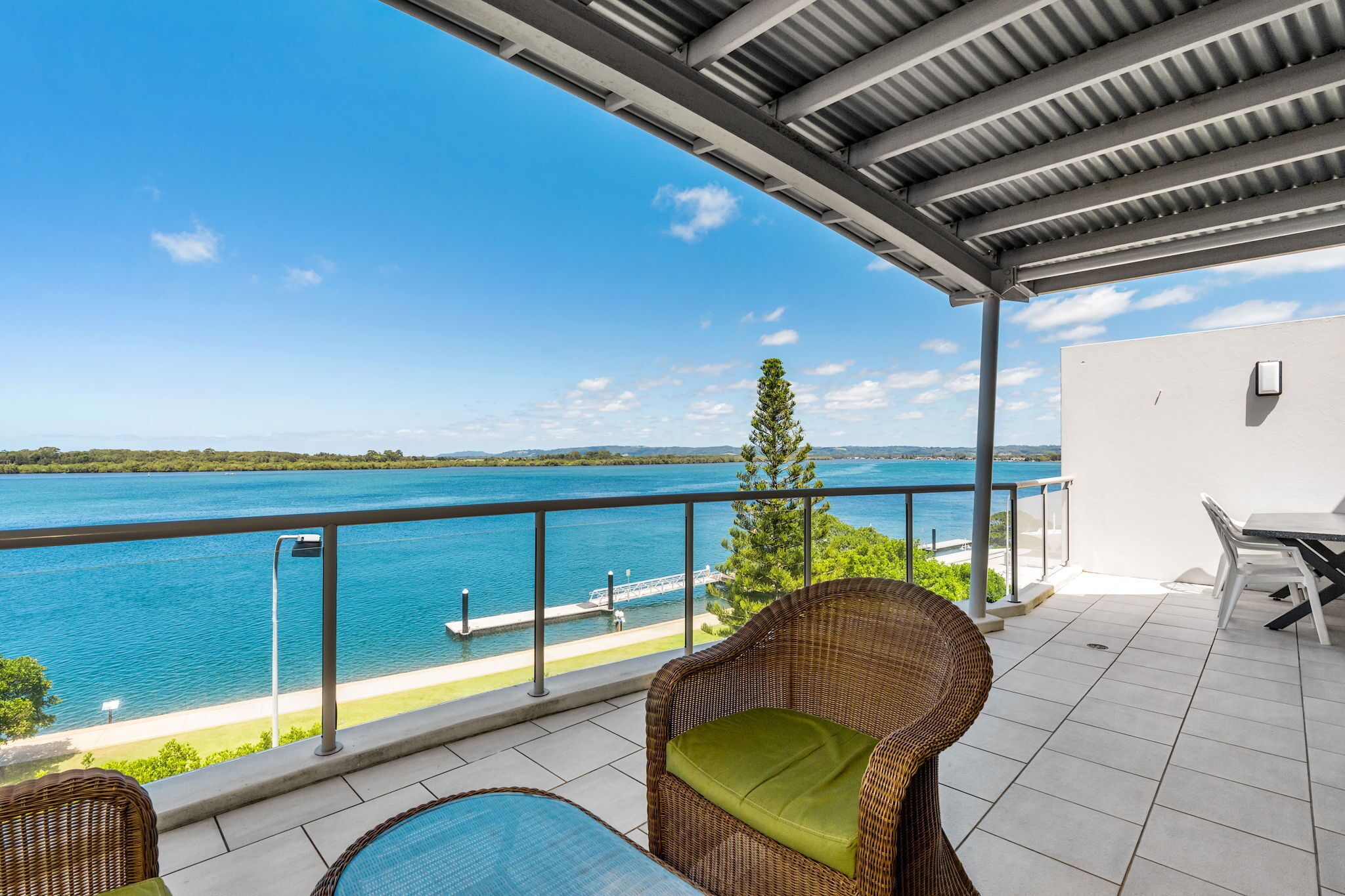 A balcony with a view of a lake, wicker furniture, and a table.