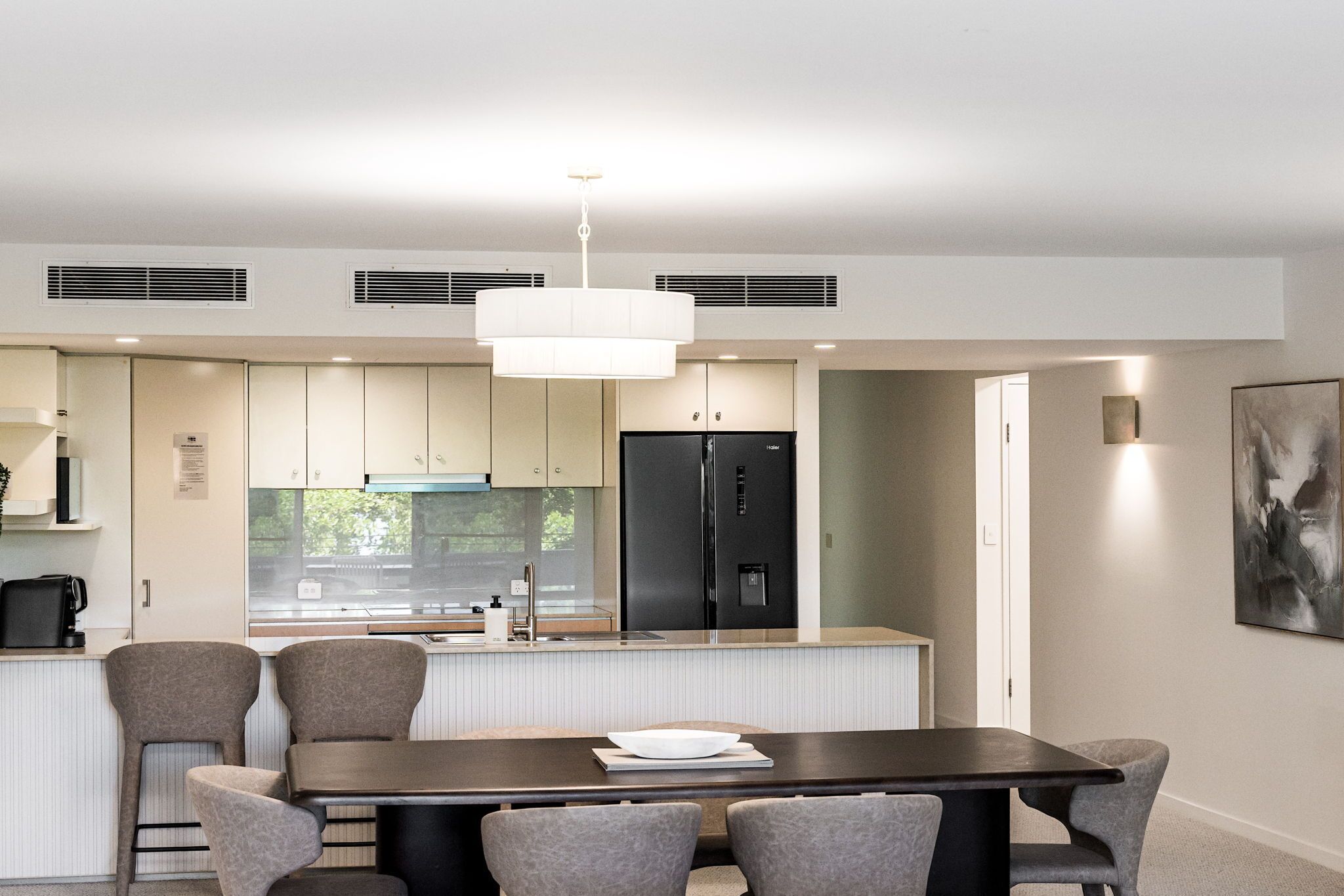 A modern kitchen with a central island, a dining area with a dark table and grey chairs, and a large abstract painting on the wall.
