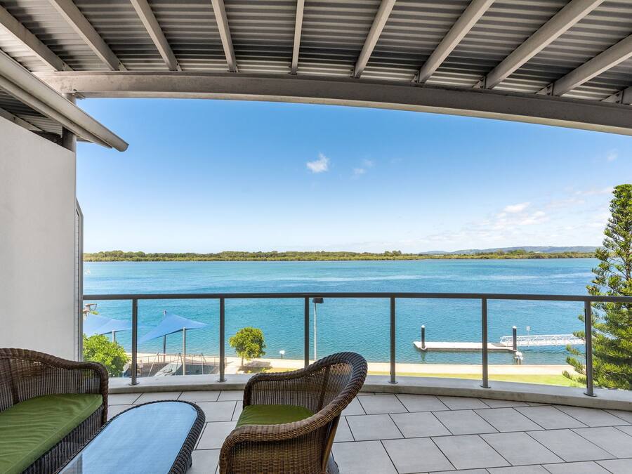A balcony with wicker furniture, a view of a lake, and a dock.