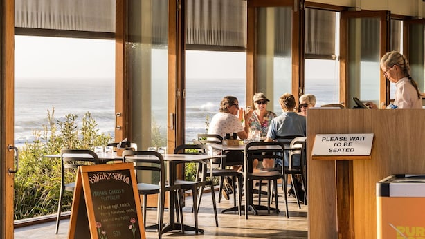 An outdoor dining area with tables and chairs, a sign indicating a special menu, and a view of the ocean. - Riverside Apartments & Hotel Ballina (Ballina)