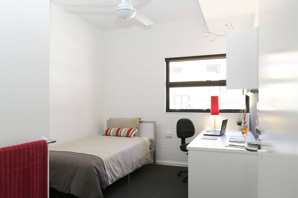 Una habitación pequeña y bien iluminada con cama, escritorio y ventana.