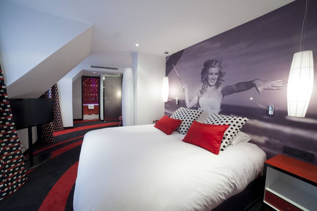 A hotel room with a large bed, red pillows, a TV, and a wall mural.