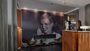 Un espace d’accueil agrémenté d’une grande fresque murale représentant un portrait, de sièges modernes et d’un comptoir d’accueil en bois.