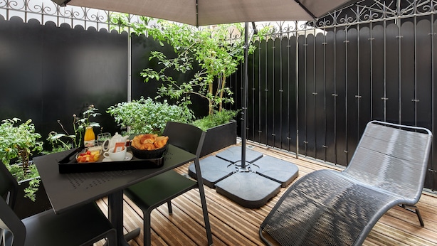 Une terrasse avec une table mise pour le petit-déjeuner, comprenant un plateau avec des toasts, des fruits et une boisson.