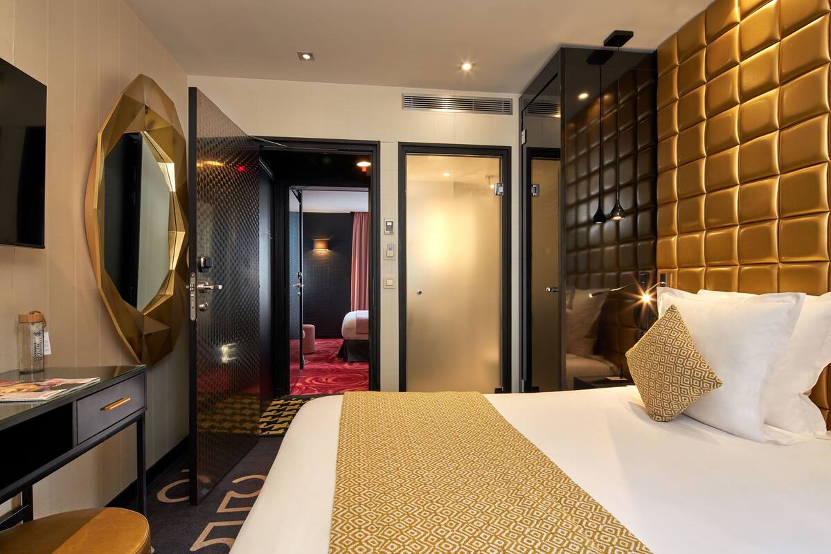 A hotel room with a large bed, a desk with a chair, a mirror, and a wardrobe.
