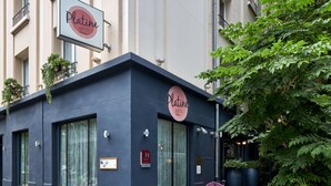 L’extérieur d’un hôtel, avec une façade sombre, de grandes fenêtres et des places assises en plein air.