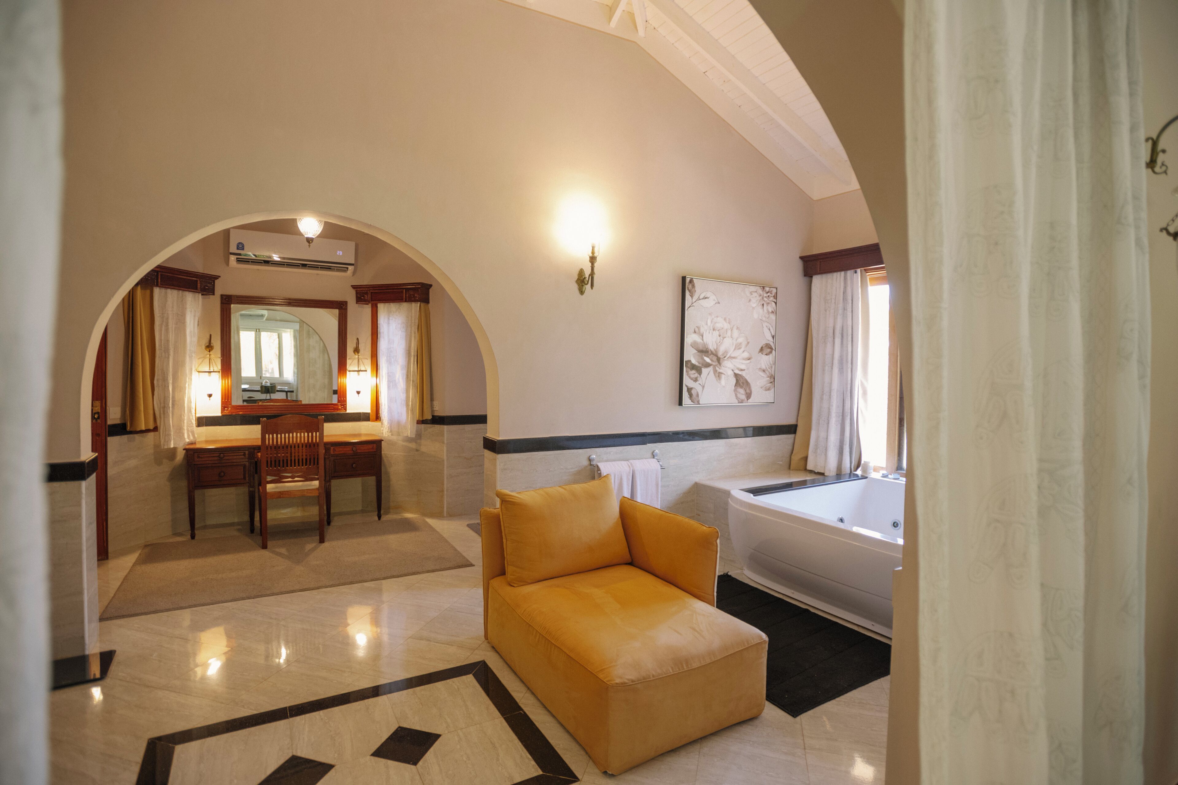 Quarto de hotel com sofá, escrivaninha, cadeira, banheira e um espelho grande.