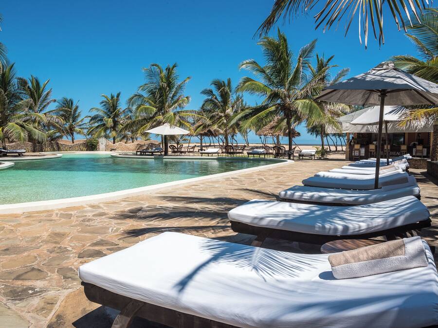A poolside area with lounge chairs and umbrellas, surrounded by palm trees.
