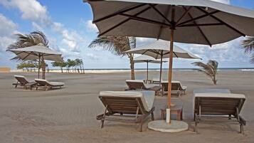 A beach with lounge chairs and umbrellas, a palm tree, and the ocean in the background.