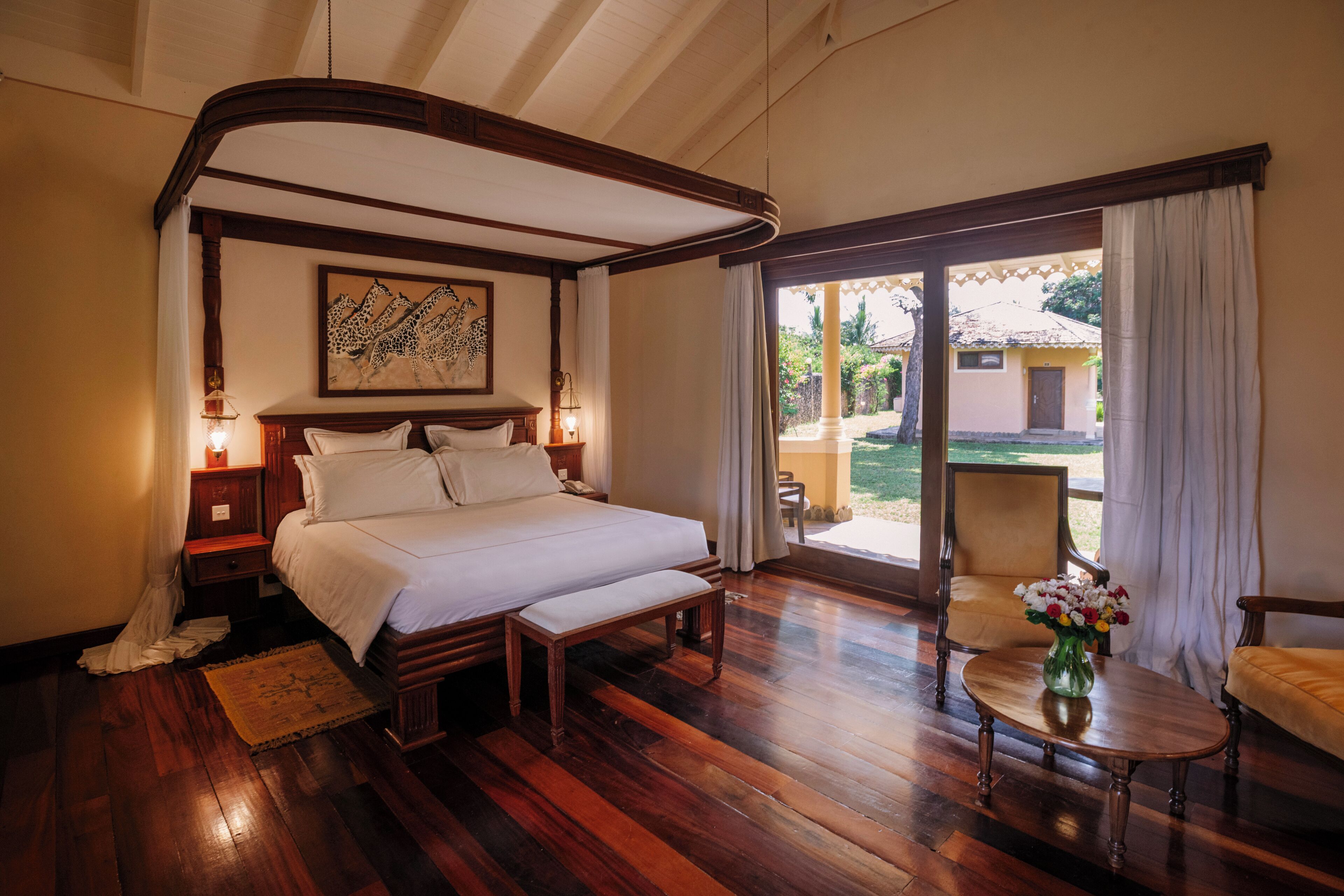 Un dormitorio con una cama grande, suelo de madera, una mesita de noche y una silla, con vistas al exterior.