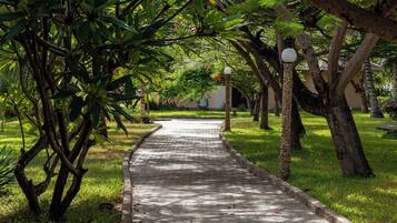 A paved pathway flanked by lush greenery and trees, leading to a building with a light-colored facade.