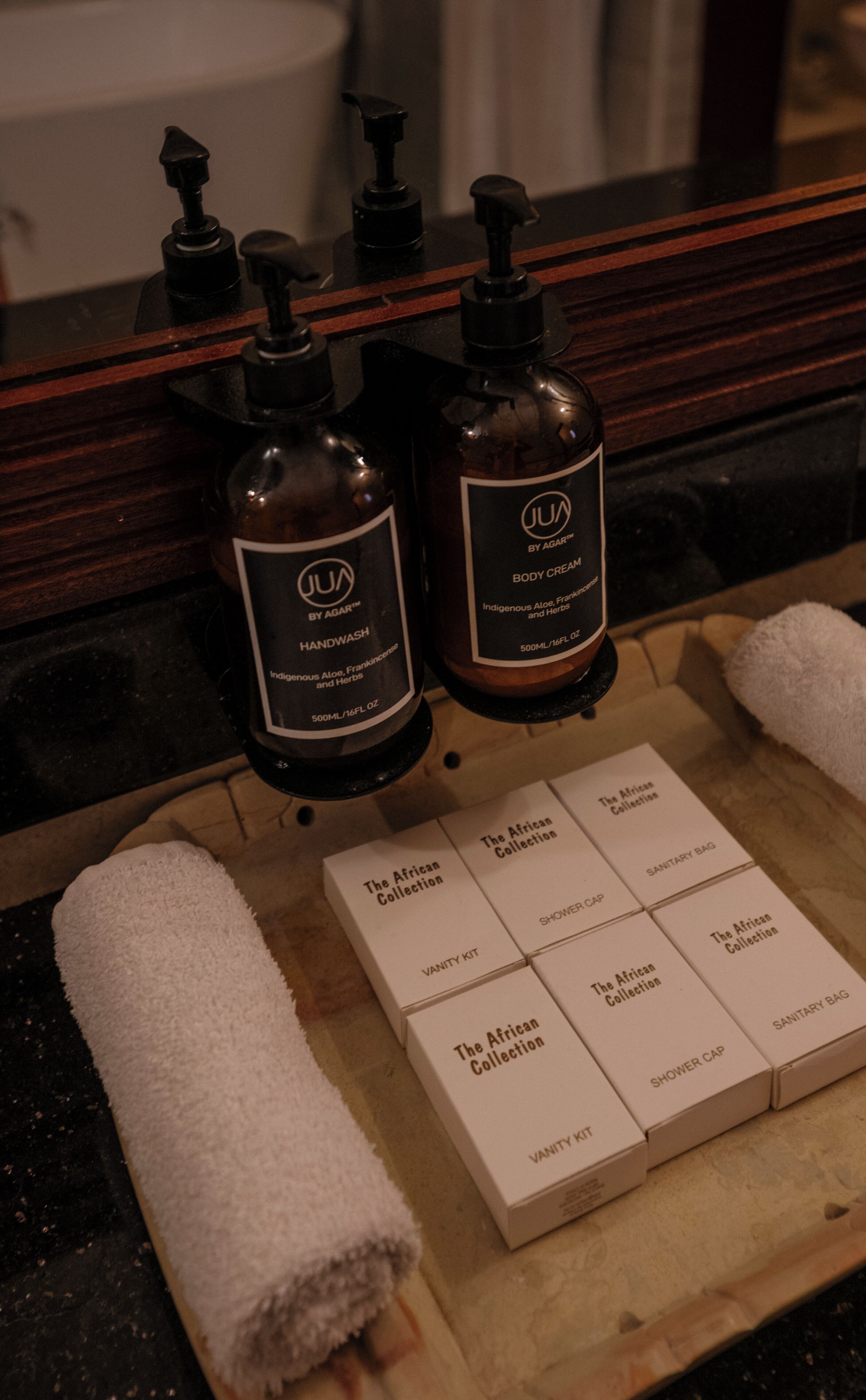 A bathroom vanity with two bottles of JUA body cream, a vanity kit, and a shower cap.