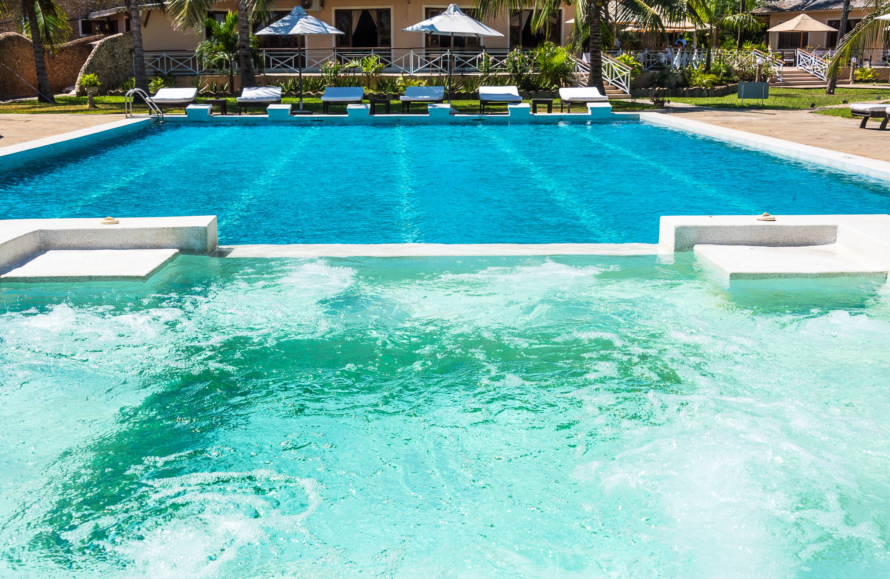 A swimming pool with clear blue water, lounge chairs, and umbrellas.