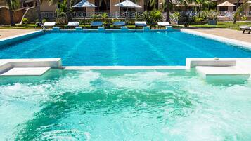 A swimming pool with clear blue water, lounge chairs, and umbrellas.