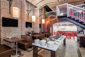 Ein Restaurant mit Backsteinwänden, Holzbalken und einer Treppe, die in einen oberen Bereich führt. Tische und Bänke sind zum Essen angeordnet.