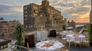 A rooftop restaurant with round tables set for dining, overlooking a cityscape with historic buildings. - TRYP by Wyndham New York City Times Square / Midtown (New York)