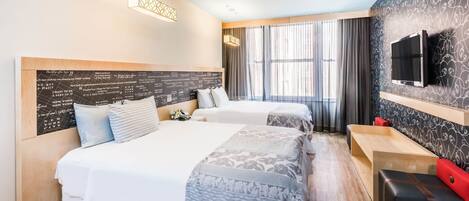A hotel room with two beds, a TV mounted on the wall, and a window with curtains.