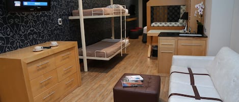 A compact hotel room with bunk beds, a sofa, a small table, a TV, and a wooden dresser.