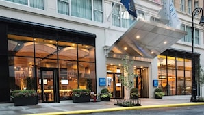 A hotel entrance with a glass facade, a covered entrance area, and a flag. - TRYP by Wyndham New York City Times Square / Midtown (New York)