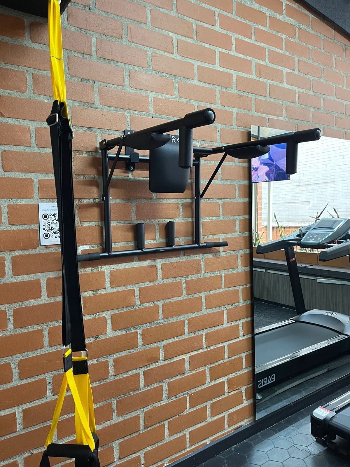 Tiiliseinä, jossa on ikkuna, juoksumatto ja leuanvetotanko.
