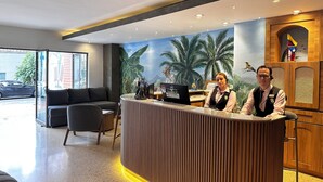 Una recepción con dos empleados, un mural de paisaje tropical y un diseño interior moderno.