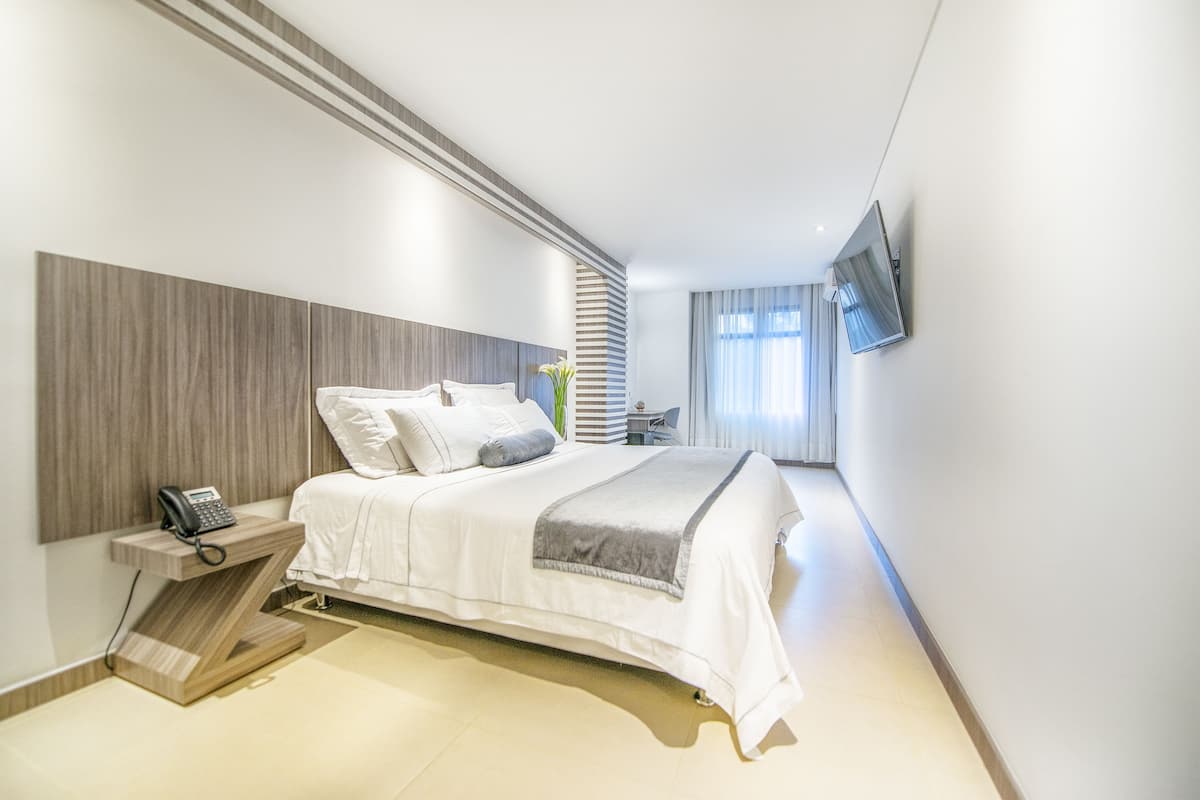 Una habitación de hotel moderna con cama, mesita de noche, teléfono y televisión montada en la pared.