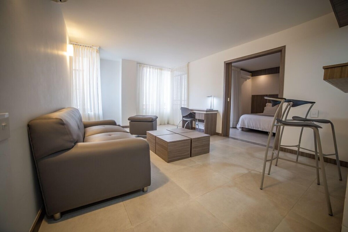 A modern hotel room with a sofa, a desk, a chair, and a bed.