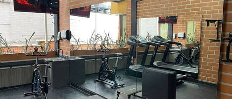 Un gimnasio con equipo de ejercicio, televisión y pared de ladrillo.
