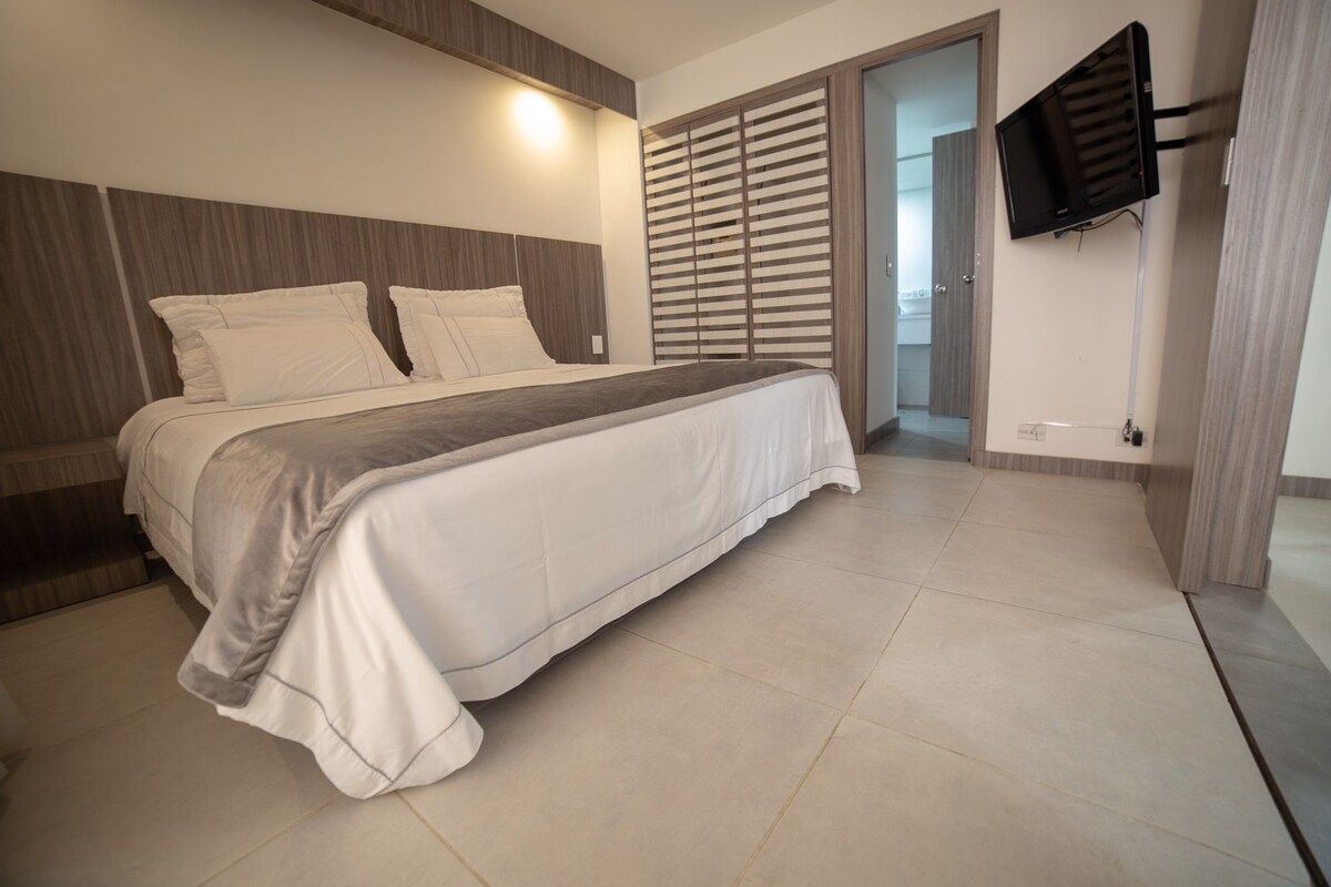 A modern bedroom with a large bed, a TV mounted on the wall, and a sliding door closet.