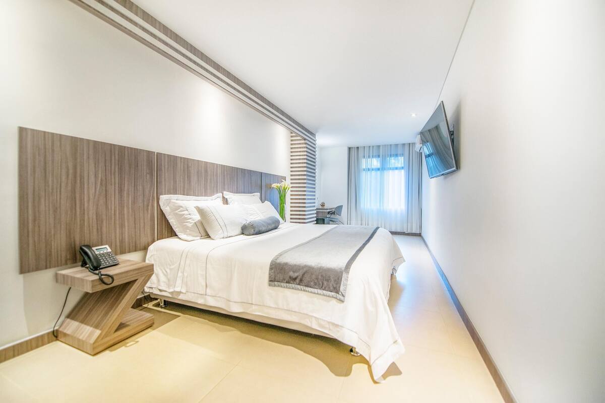 Una habitación de hotel moderna con cama, teléfono en la mesita de noche y televisión montada en la pared.