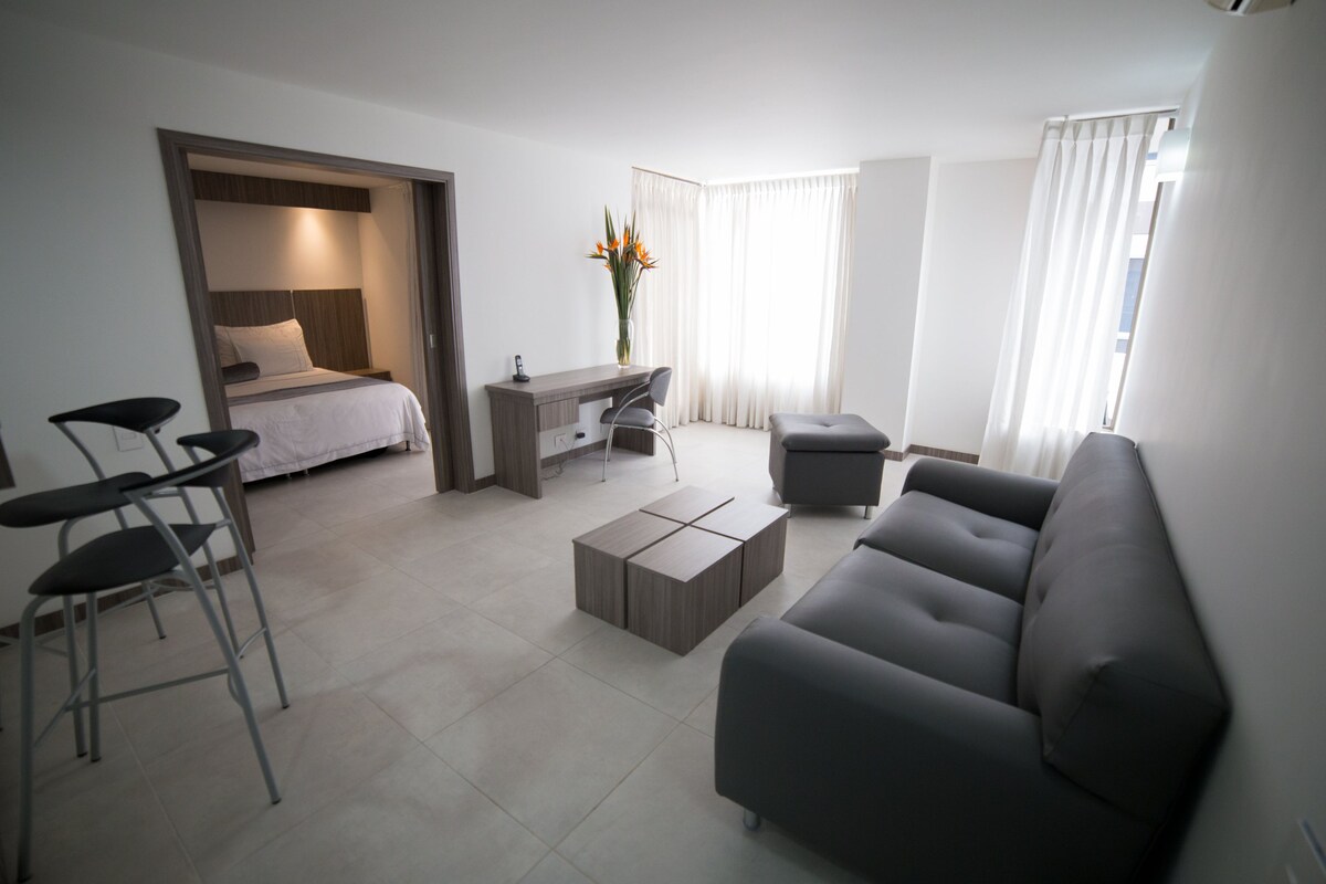 A modern hotel room with a bed, a desk, a sofa, and a coffee table.