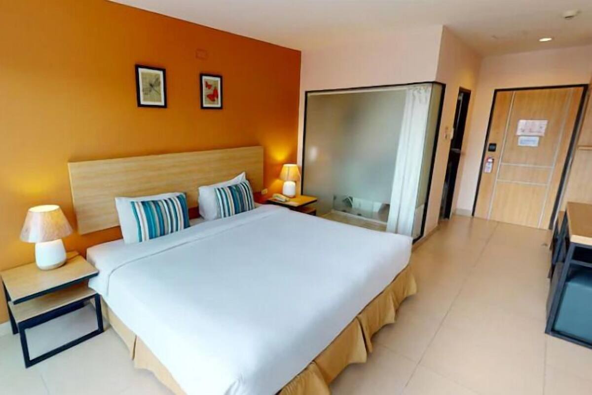 A hotel room with a large bed, two bedside tables with lamps, a wardrobe, and a door.