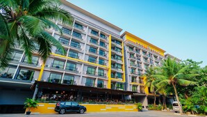 A multi-story hotel with balconies, a yellow facade, and palm trees.