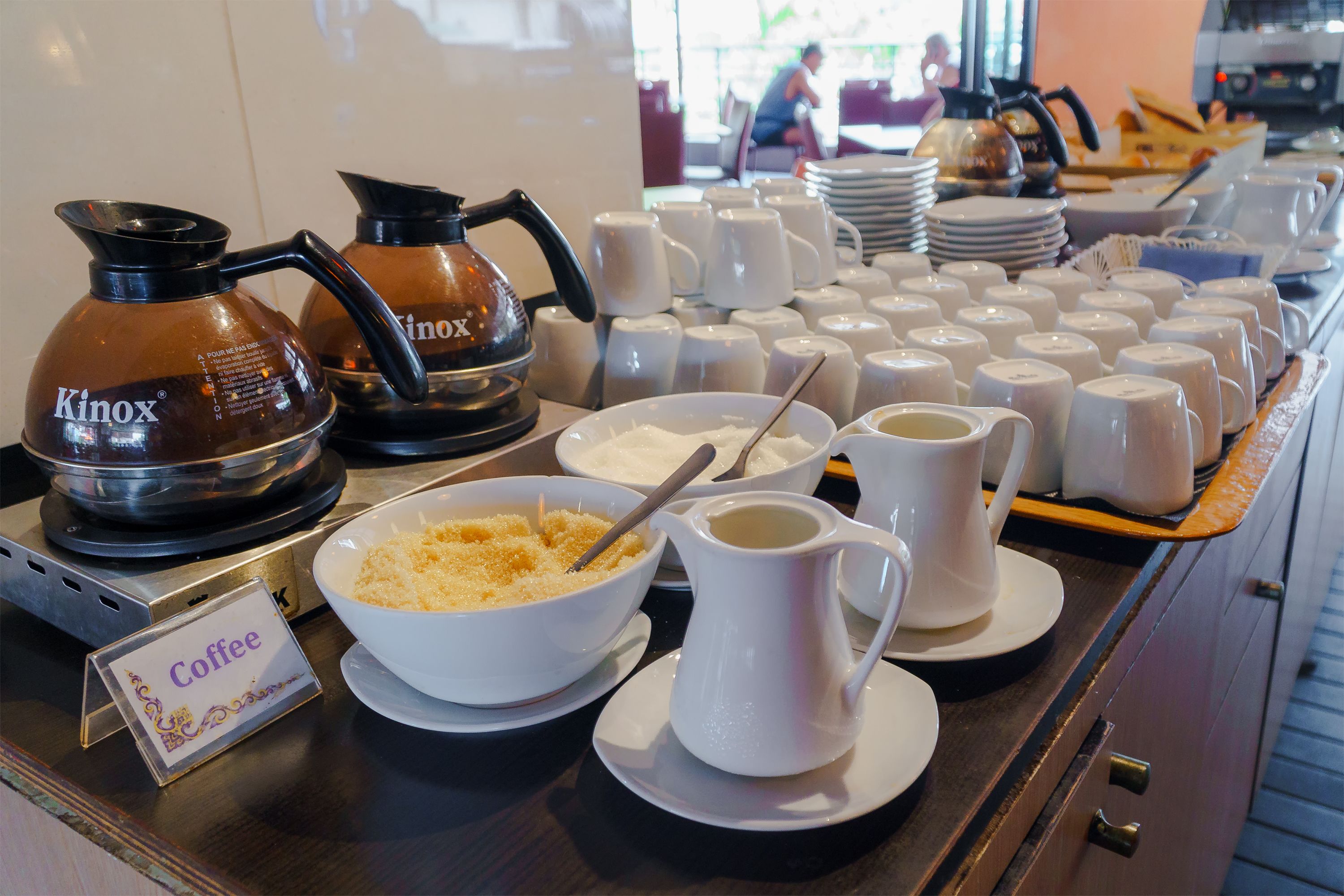 A coffee station with KINOX coffee makers, a bowl of cereal, and a pitcher of coffee.