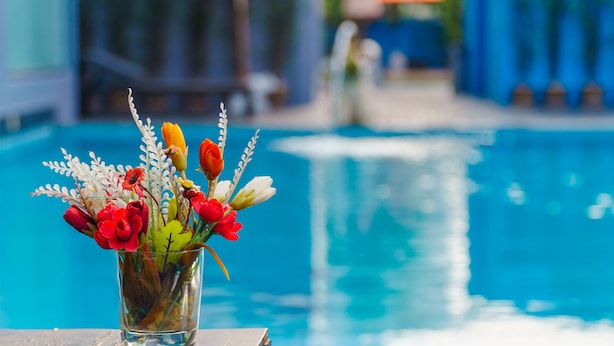A glass vase with flowers on a poolside table.