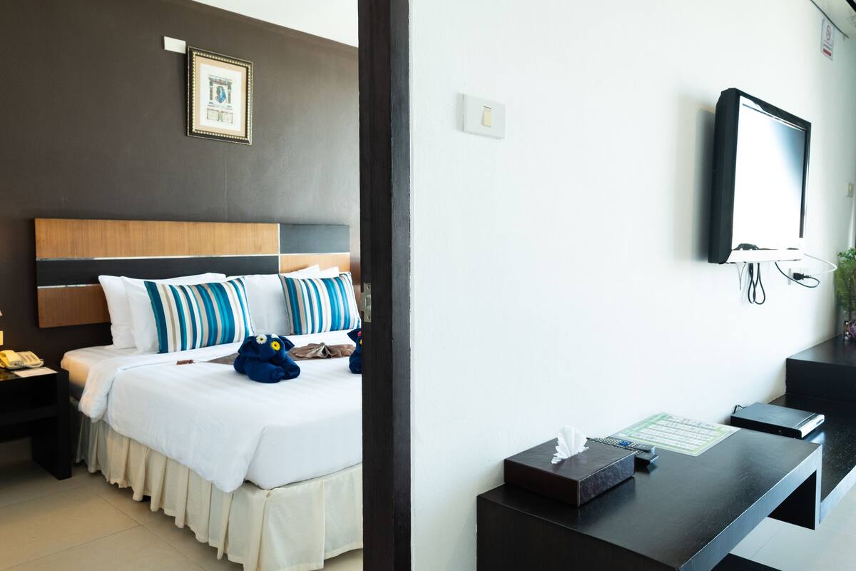 A hotel room with a bed, bedside table, and a desk with a computer and a telephone.