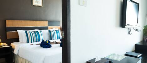 A hotel room with a bed, bedside table, and a desk with a computer and papers.