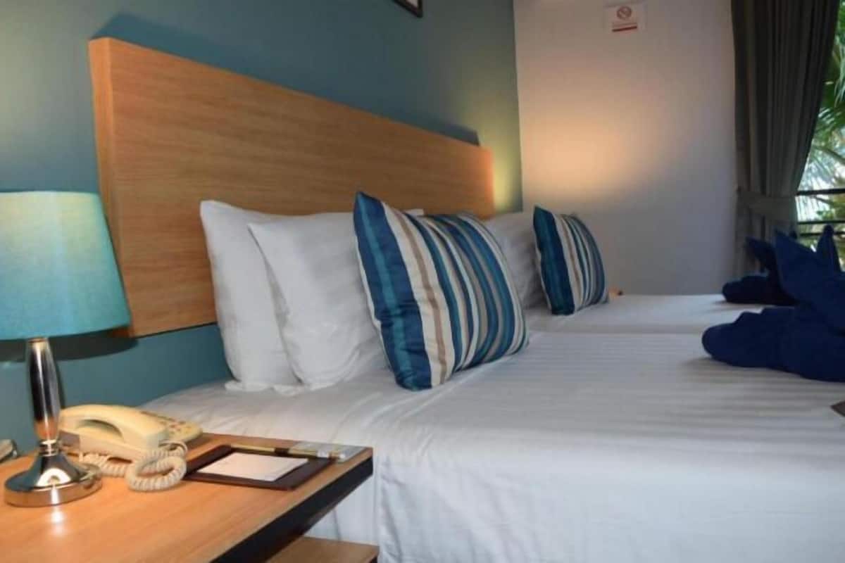 A hotel room with a wooden headboard, a bedside table with a lamp and phone, and a bed with striped pillows.