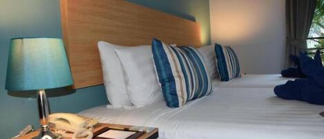 A hotel room with a wooden headboard, a bedside table with a lamp and phone, and a bed with striped pillows.