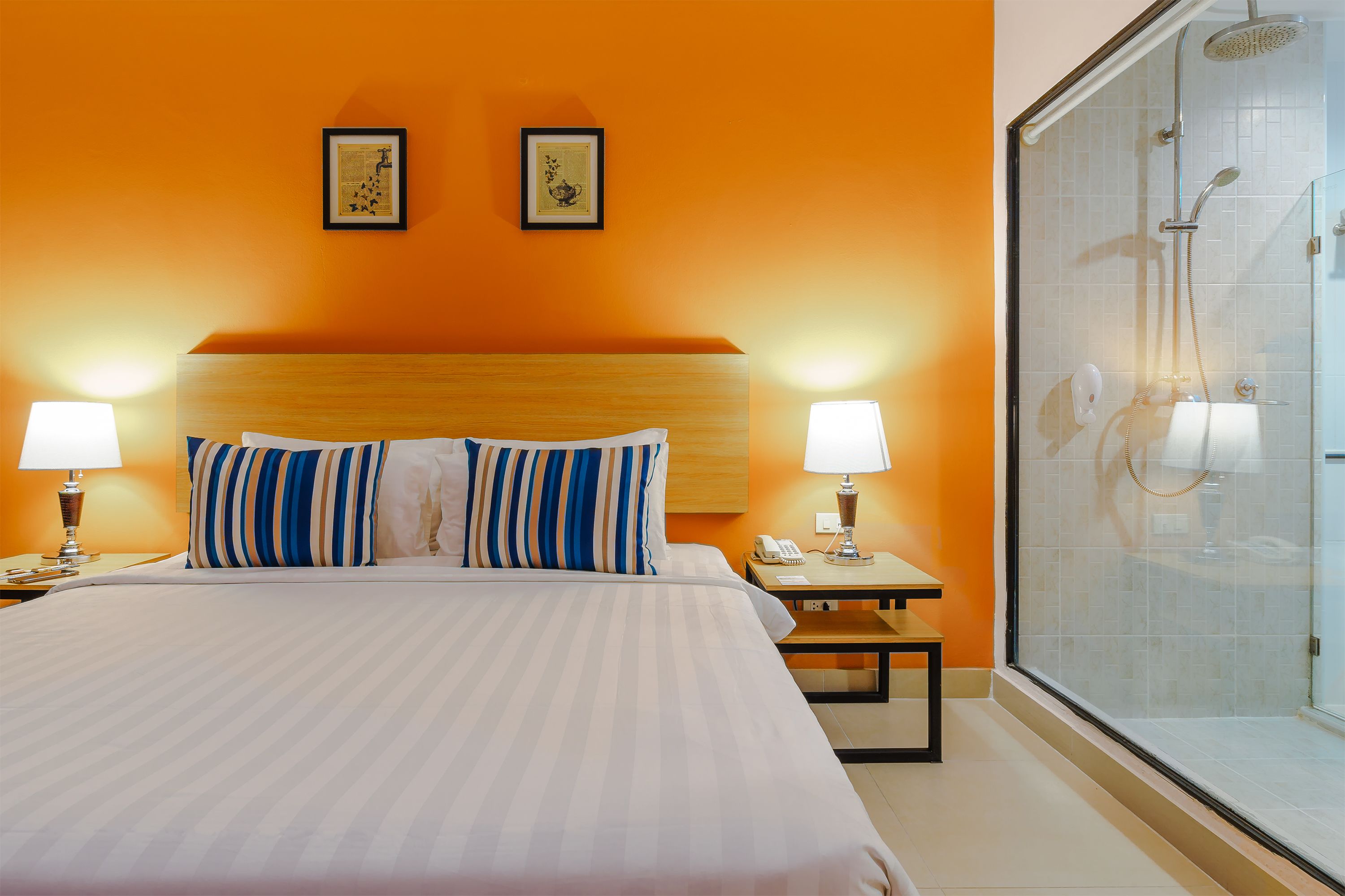 A hotel room with a large bed, two bedside lamps, a nightstand, a framed picture on the wall, and a glass shower enclosure.