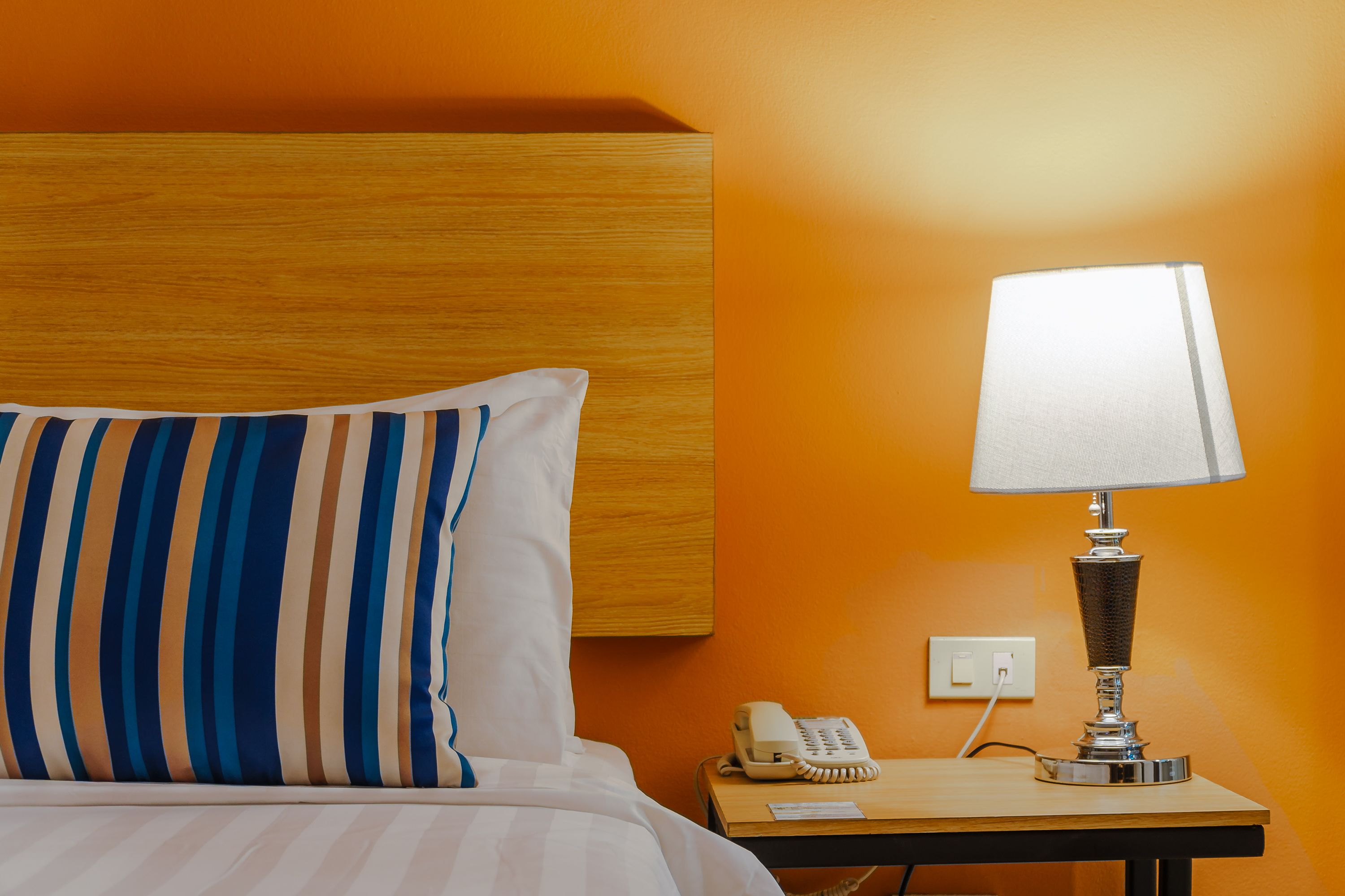 A hotel room with a striped pillow, a bedside lamp, a telephone, and a wooden nightstand.