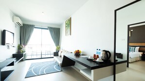 A modern hotel room with a kitchen area, a dining table, and a large window with curtains.