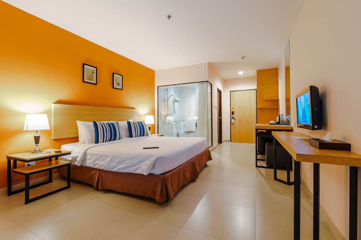 A hotel room with a bed, bedside table, lamp, and a TV on a desk.