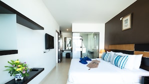 A modern hotel room with a large bed, a flat-screen TV, a vase of flowers, and a view into the bathroom.